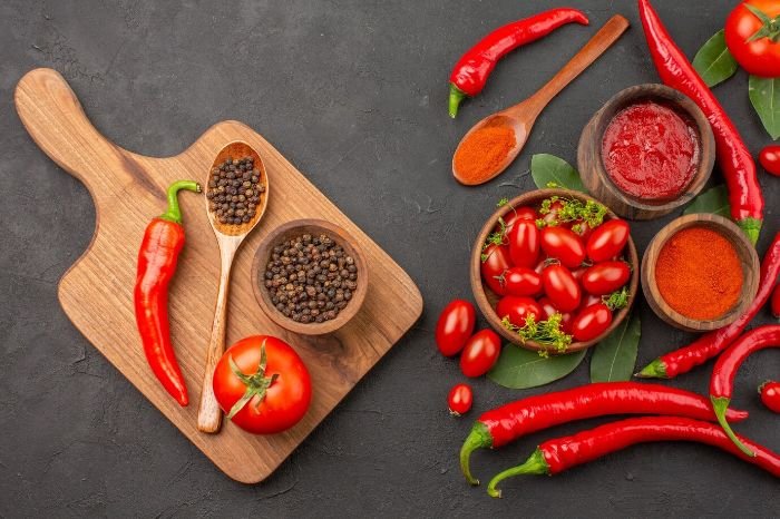 Chili peppers, tomatoes, and spices on a wooden board and dark background, highlighting the heart health benefits of capsaicin, including improved blood flow and cholesterol reduction.