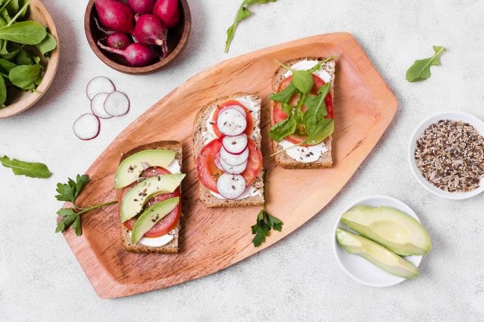 A wooden platter with radish-topped toast, avocado slices, and greens, highlighting the versatility of radishes in cooking. Roasting or sautéing radishes brings out their milder and sweeter flavors.