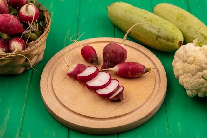 Sliced radishes on a wooden plate surrounded by fresh vegetables, highlighting the antioxidant properties of radishes that help fight free radicals and protect cells.