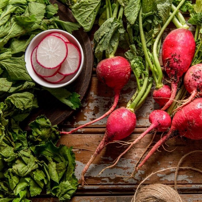 Fresh radishes with greens and sliced radishes in a bowl, showcasing their skin health benefits, including hydration and anti-inflammatory properties that soothe skin irritations and reduce redness.