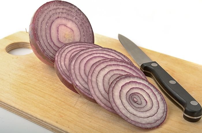 Sliced red onions on a wooden cutting board, highlighting their anti-inflammatory properties due to the antioxidant quercetin.