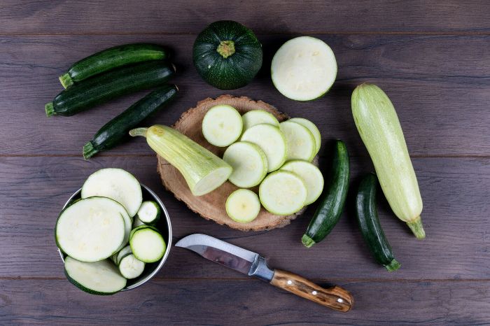 Various zucchini types and slices arranged on a wooden surface, highlighting the vegetable's vitamin C and beta-carotene content that support skin health by boosting collagen production and fighting free radicals.