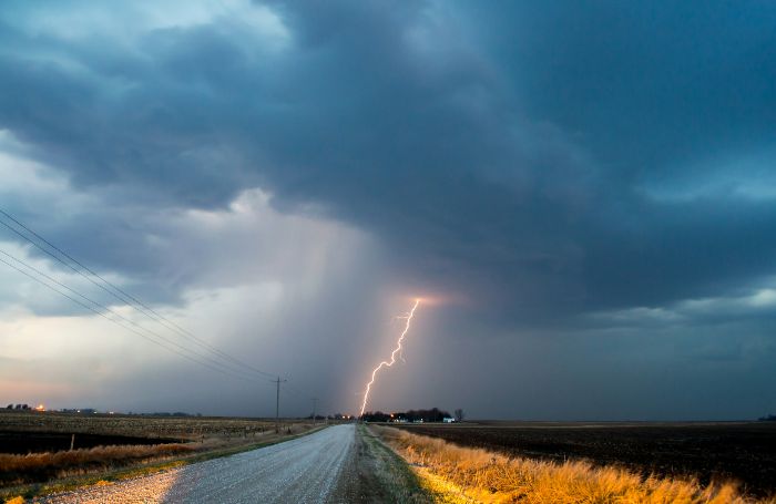Lightning strikes in the distance under dark storm clouds, highlighting the challenges of unpredictable weather patterns and their impact on watering schedules.