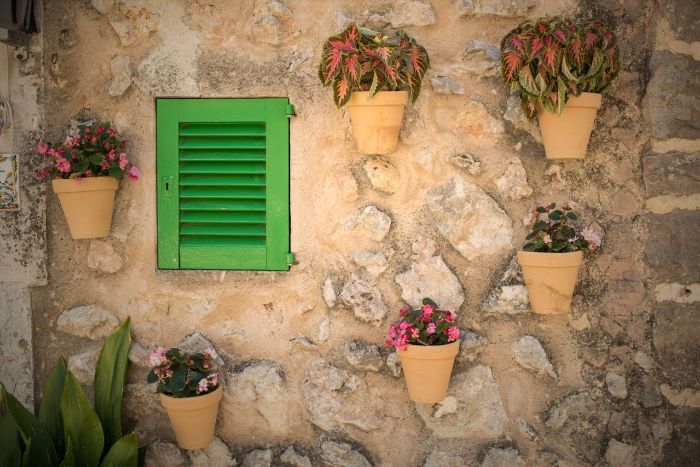 Various hanging planters attached to a stone wall beside a green window, showcasing an example of vertical garden structures.