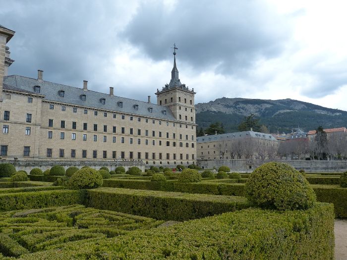 Symmetrical formal garden design featuring well-trimmed boxwood hedges and topiary against the backdrop of a historic building.