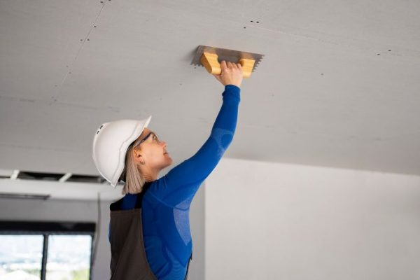 A construction worker in safety gear repairing drywall with a trowel, illustrating the fundamentals of drywall repair techniques and tools.