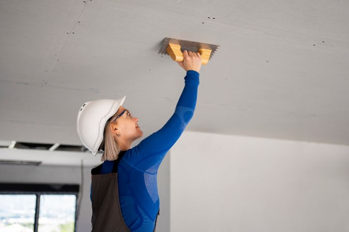 A construction worker in safety gear repairing drywall with a trowel, illustrating the fundamentals of drywall repair techniques and tools.