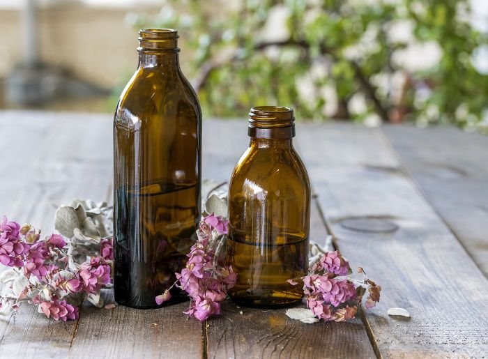 Empty amber glass bottles with dried flowers, perfect for creating DIY stress-relief essential oil blends.