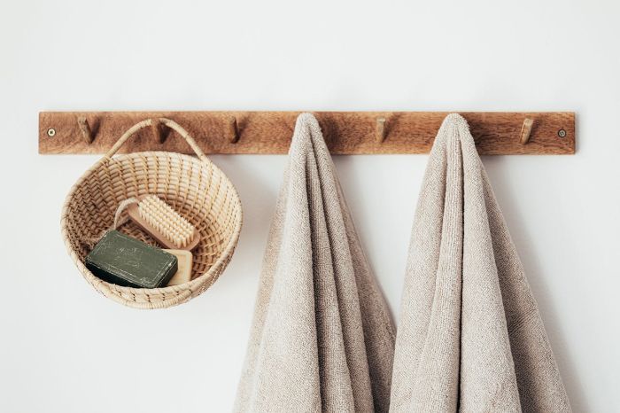 Wooden wall rack with hooks holding beige towels and a wicker basket containing soap and brushes, showcasing an efficient door storage solution for small bathrooms.