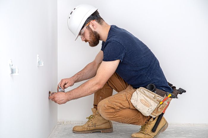 A construction worker in a hard hat fixing cracks in a drywall-repaired area using a tool for better adhesion of the compound.