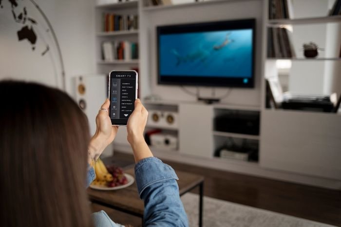 Person using a smartphone to control a smart TV with voice commands, demonstrating the convenience of smart assistants like Google Assistant and Alexa.