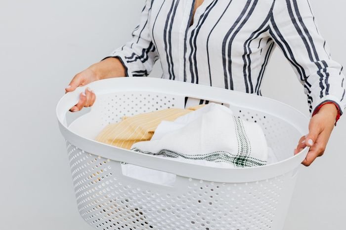 A person holding a white laundry basket filled with neatly folded clothes, symbolizing natural and chemical-free laundry care with homemade detergent and stain remover solutions.