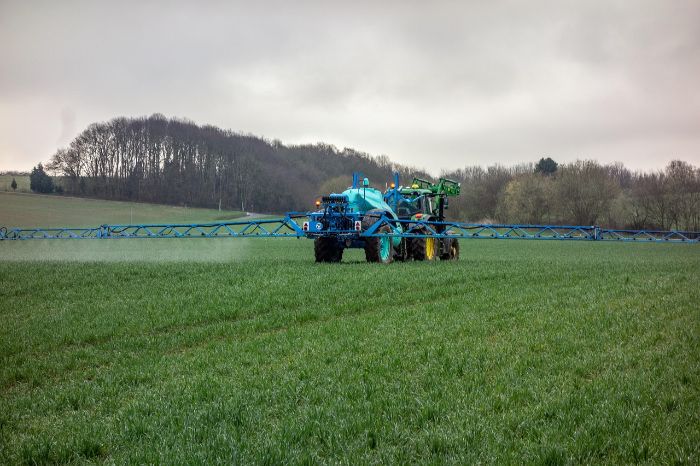 Tractor applying fertilizer to a large field, illustrating the potential risk of overfertilization and the importance of taking immediate corrective steps in garden care.