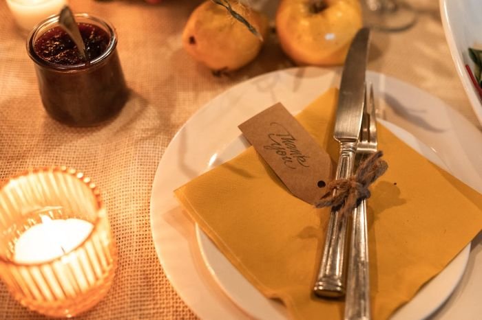 Elegant table setting with yellow napkins, vintage silverware tied with twine, a "Thank You" tag, and cozy lighting, perfect for an intimate dinner party.