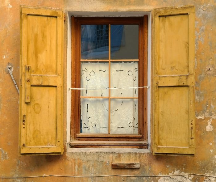 An old wooden window with yellow shutters, illustrating how outdated windows contribute to energy loss and highlighting the benefits of switching to energy-efficient alternatives to reduce energy consumption and carbon footprint.