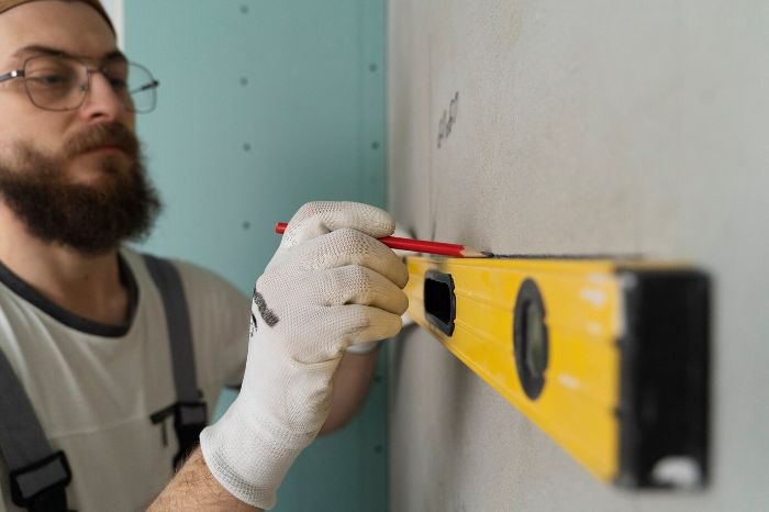 A man using a yellow level and pencil to measure and mark a drywall patch area, illustrating the step-by-step process for patching drywall effectively.
