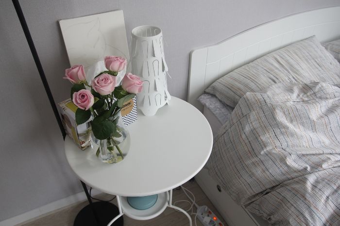 Organized bedroom with a tidy bedside table and fresh pink roses in a vase, representing daily habits for maintaining home cleanliness.