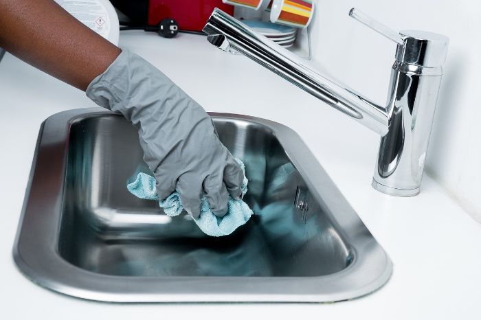 Person wearing gloves wiping down a stainless steel sink, demonstrating the one-minute rule for quick tidying and maintaining a clean home.