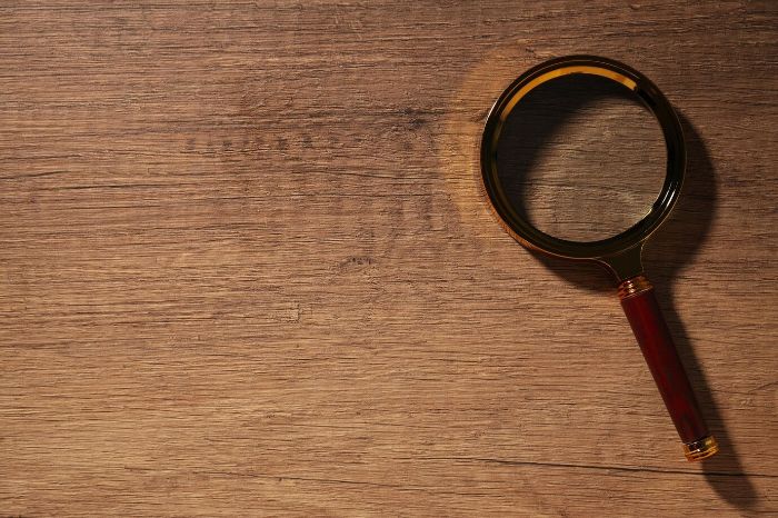 Magnifying glass on a wooden surface, representing tools like magnifiers and white paper used to detect spider mites in plants.