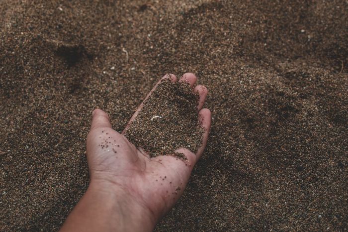 Hand holding sandy soil, illustrating methods to improve water retention by adding compost, topsoil, and organic materials.