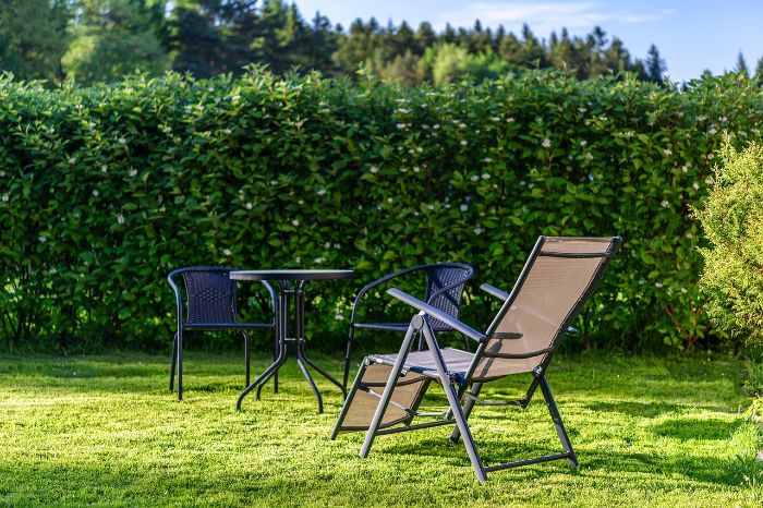 Outdoor garden with chairs and table in front of tall, thick hedges, demonstrating the ideal height and thickness for wind protection and noise reduction.