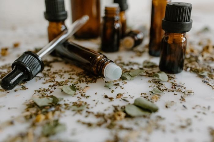 Close-up of amber essential oil bottles surrounded by dried jasmine leaves, illustrating how jasmine oil can be used in diffusers, candles, and potpourri to create a welcoming and fragrant home environment.