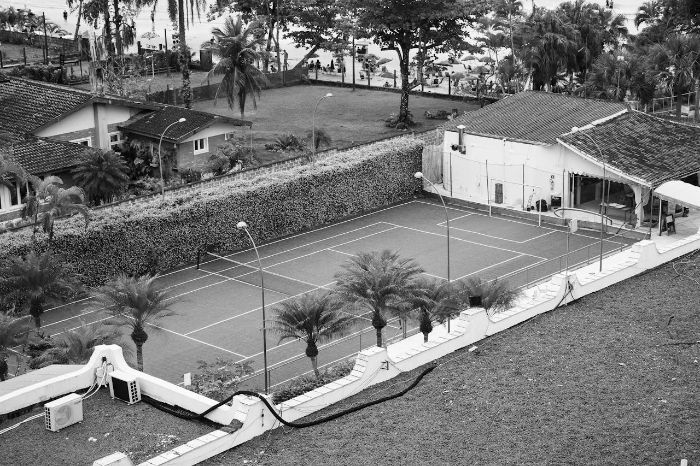 Black-and-white image of a tennis court surrounded by well-maintained hedges, illustrating the role of planting and care in creating wind-reducing barriers.