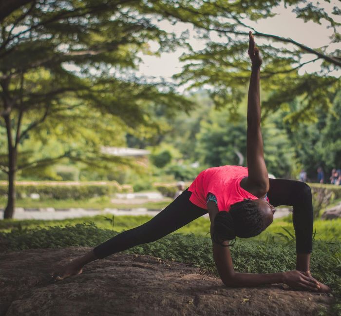 Person stretching outdoors in a garden-like setting, symbolizing how gardening activities can improve physical flexibility and body movement.