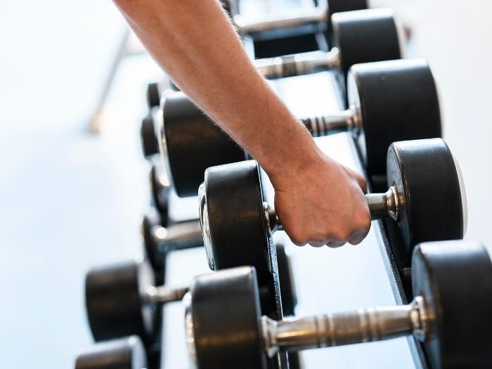 Close-up of a person picking up a dumbbell in a gym, symbolizing the integration of garden work into a regular fitness routine for strength and health benefits.