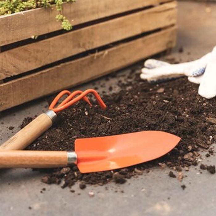 Hand tools and fresh soil next to a garden bed, representing the long-term benefits of mulching for plant growth and soil health.