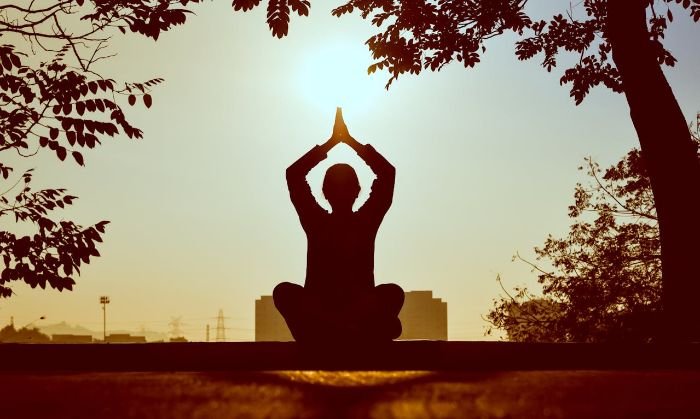 Person practicing yoga at sunrise, symbolizing the integration of yoga-inspired movements like lunges and twists into daily gardening tasks to enhance flexibility and body awareness.