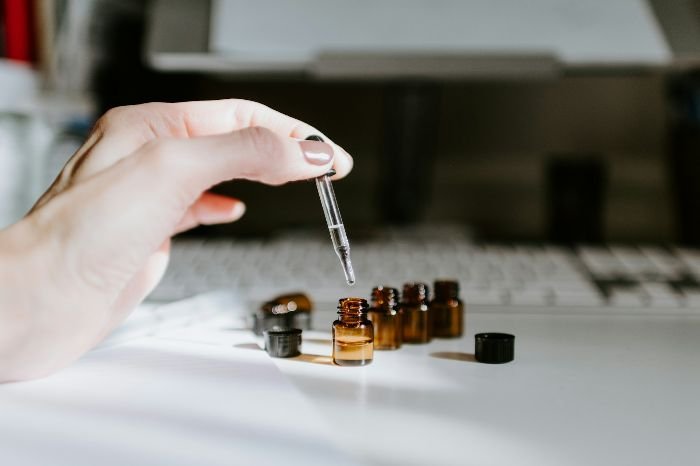 Hand holding dropper above small essential oil bottles on a white surface, representing safety precautions when using oils in homes with children and pets.