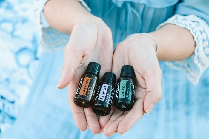 Hands holding small bottles of lavender, peppermint, and orange essential oils used for natural cleaning and aromatic home care.