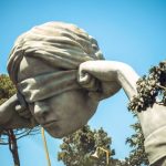 Dramatic large-scale outdoor sculpture of a blindfolded head with hands, placed among trees - illustrating how bold artistic placement can shape mood, symbolism, and spatial flow in garden landscapes.