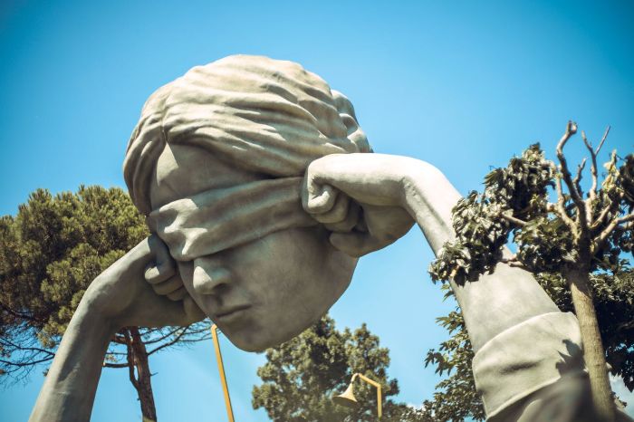 Dramatic large-scale outdoor sculpture of a blindfolded head with hands, placed among trees - illustrating how bold artistic placement can shape mood, symbolism, and spatial flow in garden landscapes.