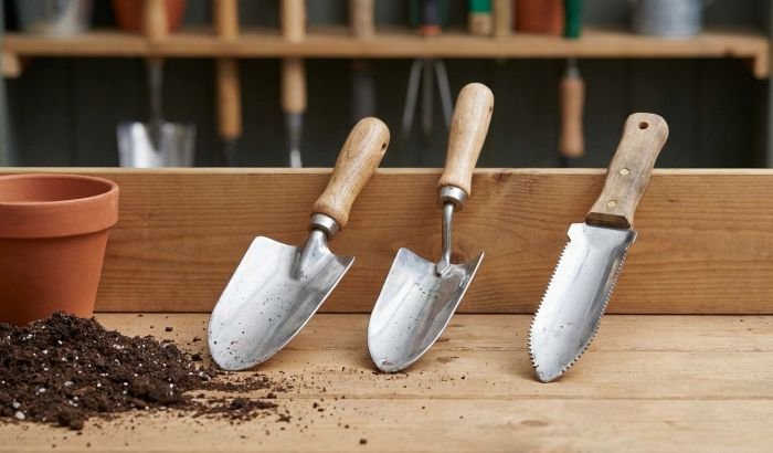 Three garden trowels with different blade shapes placed on a workbench, showing common trowel types used for planting, transplanting, and soil work