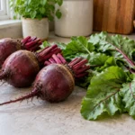 Sound red beet roots with trimmed stems and separate fresh beet greens on a kitchen counter