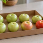 Pale green and blushing tomatoes spaced in a single layer in an open cardboard tray